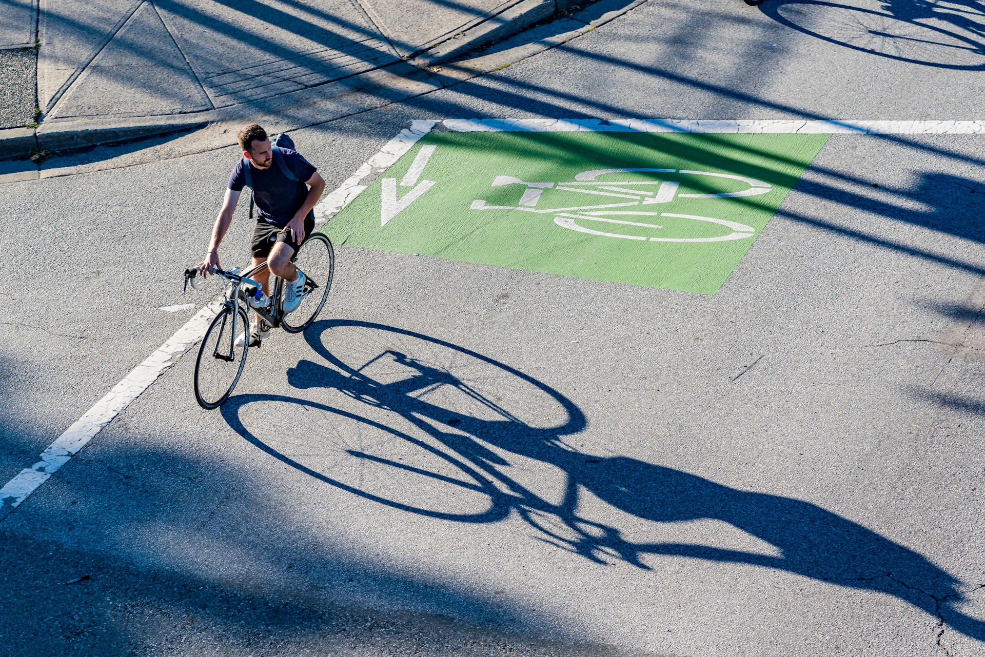 Cyclist on a road with a cyclist sign painted on it, throwing a large shadow